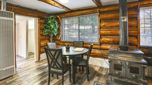A rustic cabin interior with a dining area, a large window, a wooden ceiling, and a wood-burning stove. - MTB Base Camp! Rustic Cabin By Mt Laguna Trails (Mount Laguna)