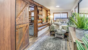 A log cabin interior with a rustic wooden door, a cozy seating area with a sofa and armchairs, and a large potted plant. - MTB Base Camp! Rustic Cabin By Mt Laguna Trails (Mount Laguna)
