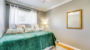 Ein Schlafzimmer mit Bett, Vorhängen, Lampe, Spiegel und Deckenventilator.
