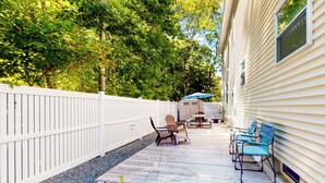 A covered patio with outdoor furniture, a white fence, and a house with siding.