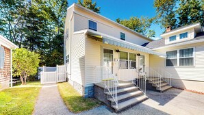 A two-story mobile home with a front porch, a small front yard, and a gravel driveway.