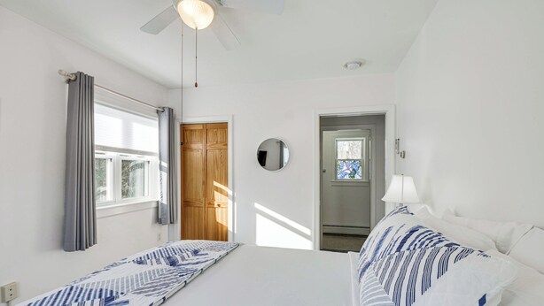 A hotel room with a bed, a ceiling fan, a window with curtains, a door, and a mirror on the wall.