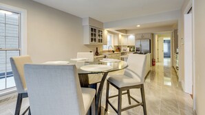 A modern kitchen with a glass dining table, white chairs, and built-in cabinets. - 7 Mi to Dtwn Toledo: Spacious Family Home! (Perrysburg)