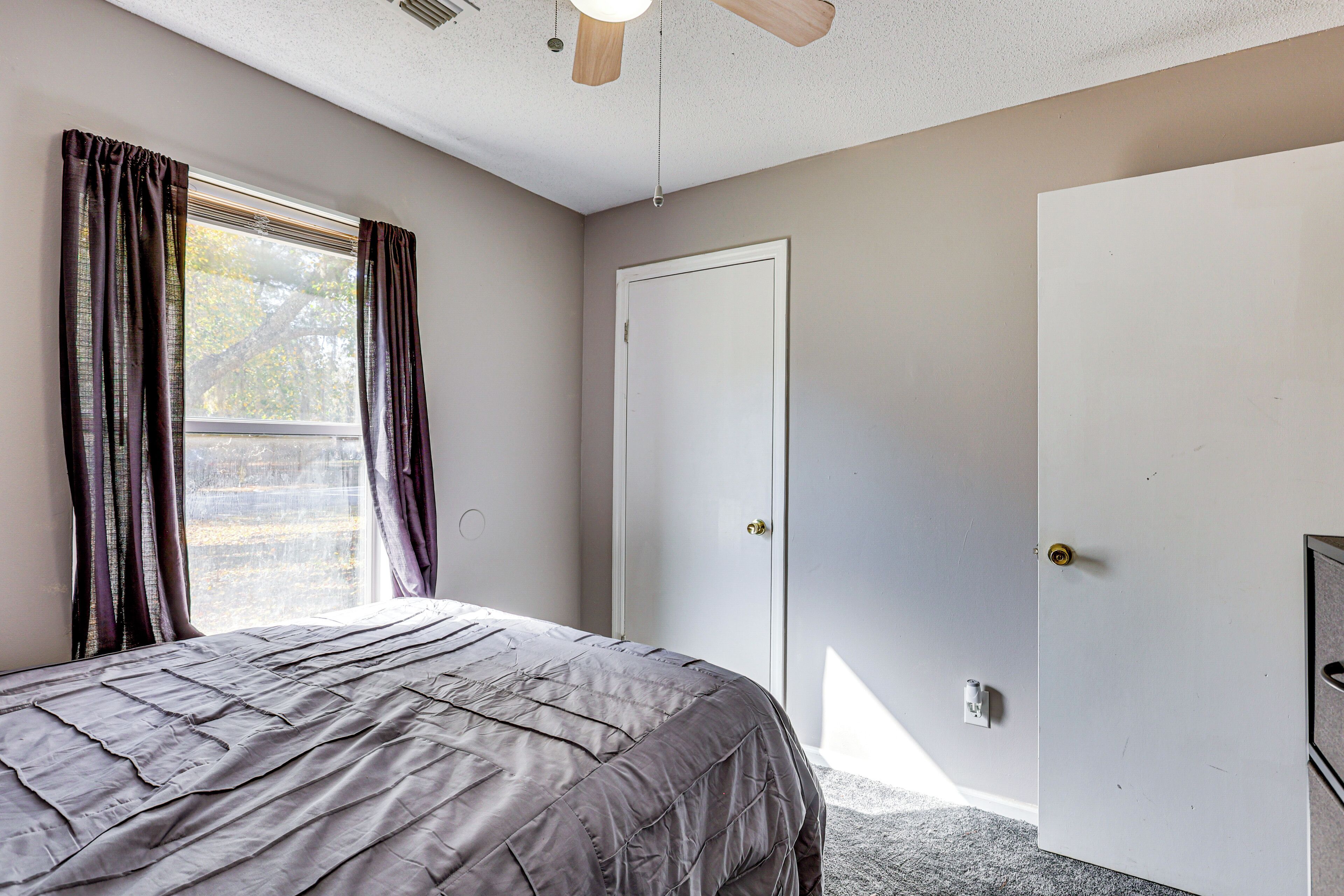 A bedroom with a bed, a door, and a window with curtains.