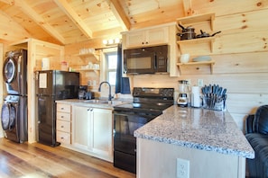 A compact kitchen with wooden cabinets, a built-in microwave, a stove, and a washing machine. - Sweet Thang: Romantic Blue Ridge Mtns Getaway (Union Mills)