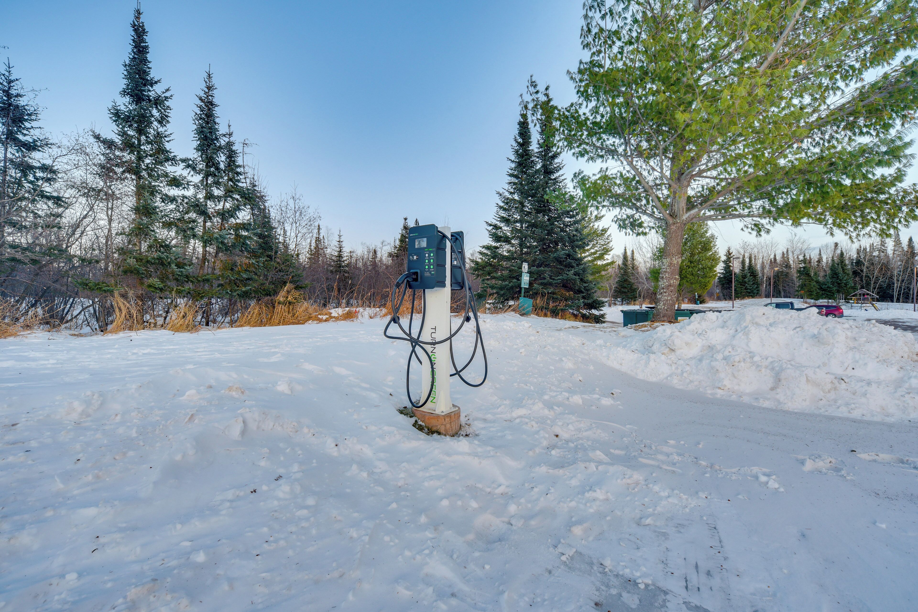 A snow-covered landscape with a charging station in the center, surrounded by trees and a clear sky.
