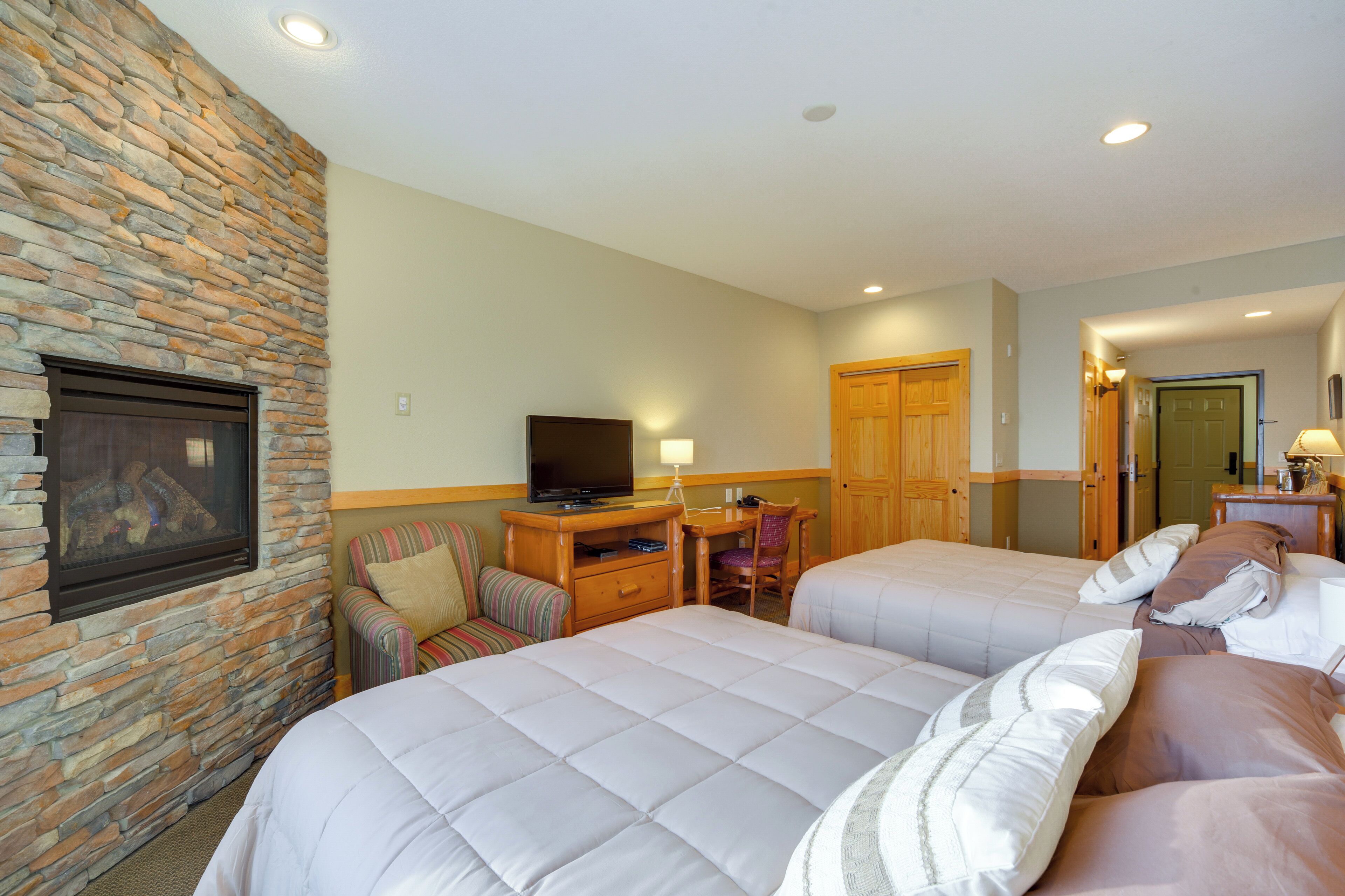 Habitación de hotel con dos camas, un televisor, un escritorio con una silla y una pared de piedra.