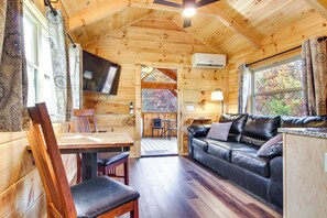 A wooden cabin interior with a wooden dining table, chairs, a leather sofa, and a television mounted on the wall. - 'feelin Feisty:' Blue Ridge Mtns Couple's Cabin (Union Mills)