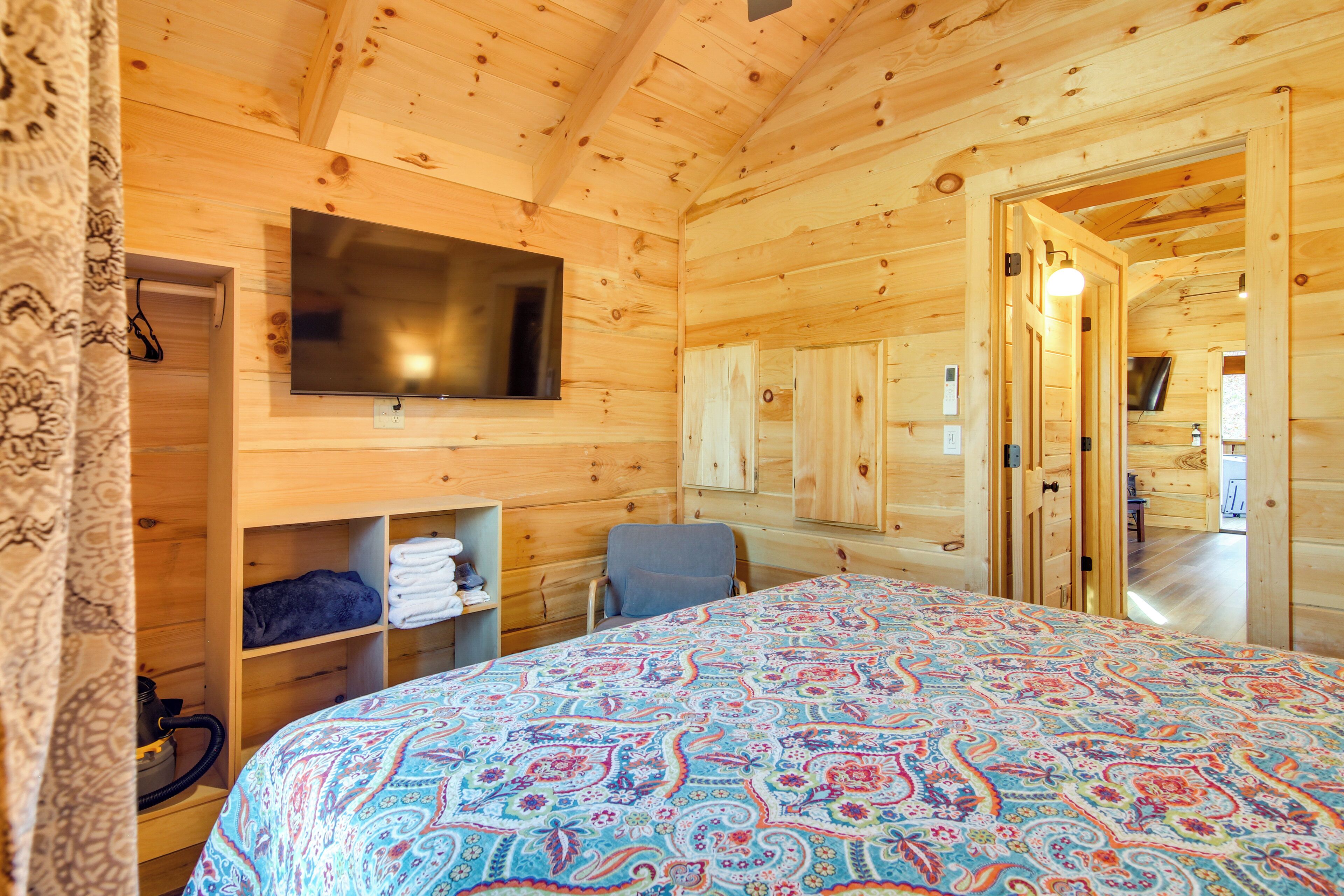 A wooden cabin room with a bed, a TV mounted on the wall, and a door leading to another room.
