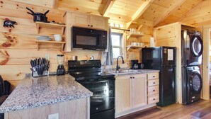 Cocina estilo cabaña de madera con encimeras de granito, estufa, microondas, fregadero y lavadora-secadora.