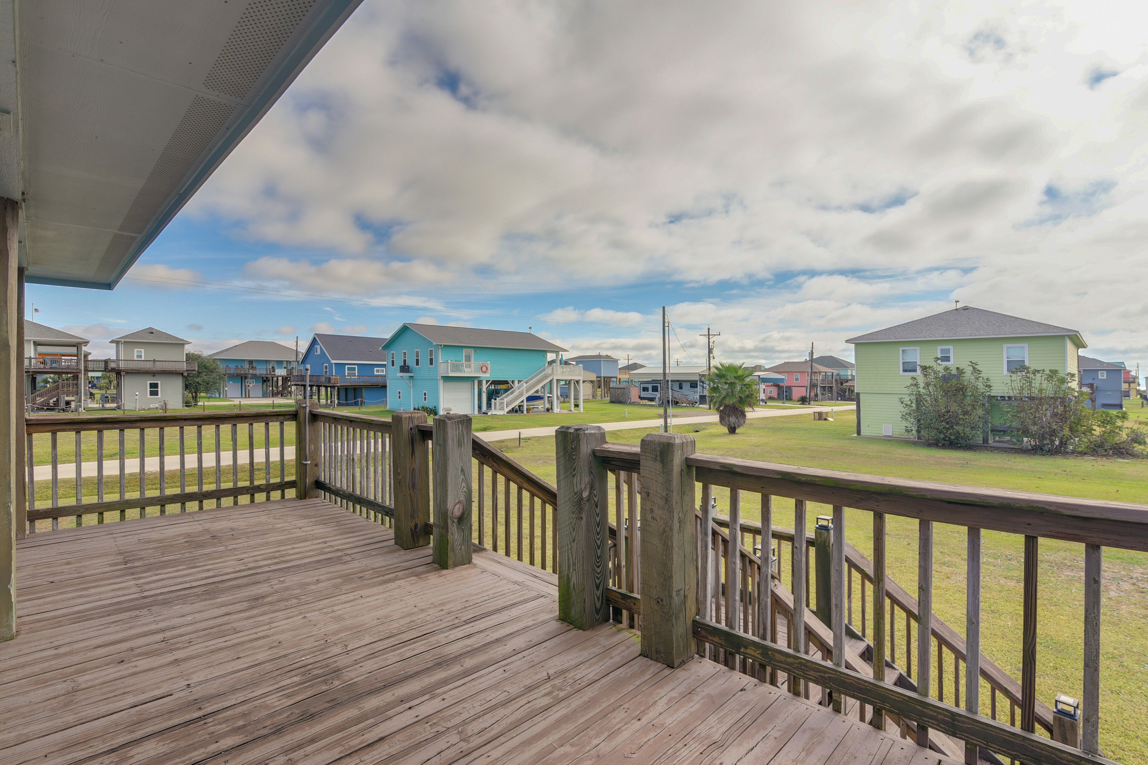 A wooden deck with a railing overlooking a residential area with houses and a grassy lawn.