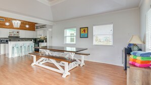A spacious kitchen with a wooden table and bar stools, a dining area with a bench, and a view of the outside through large windows. - Steps to Sea! Crystal Beach Home w/ Furnished Deck (Port Bolivar)