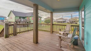 A wooden deck with a covered area, a chair, and a view of houses in the background. - Steps to Sea! Crystal Beach Home w/ Furnished Deck (Port Bolivar)