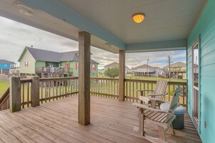 A wooden deck with a covered area, a chair, and a view of houses in the background.