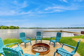 A fire pit with four Adirondack chairs arranged around it, overlooking a calm lake with a dock in the background. - Casa de Nello - Charming Family Home! (Antioch)