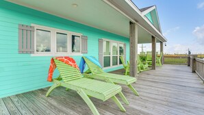 Un bâtiment turquoise doté d’une terrasse en bois, de fauteuils de jardin verts et d’un espace abrité avec une rambarde.