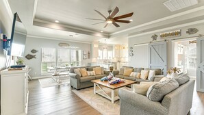 Un salon spacieux doté d’un grand ventilateur de plafond, d’une table basse en bois et d’un canapé gris.