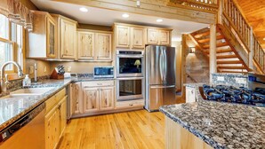 Une cuisine moderne avec des meubles en bois, des appareils électroménagers en acier inoxydable, des plans de travail en granit et un escalier en bois.