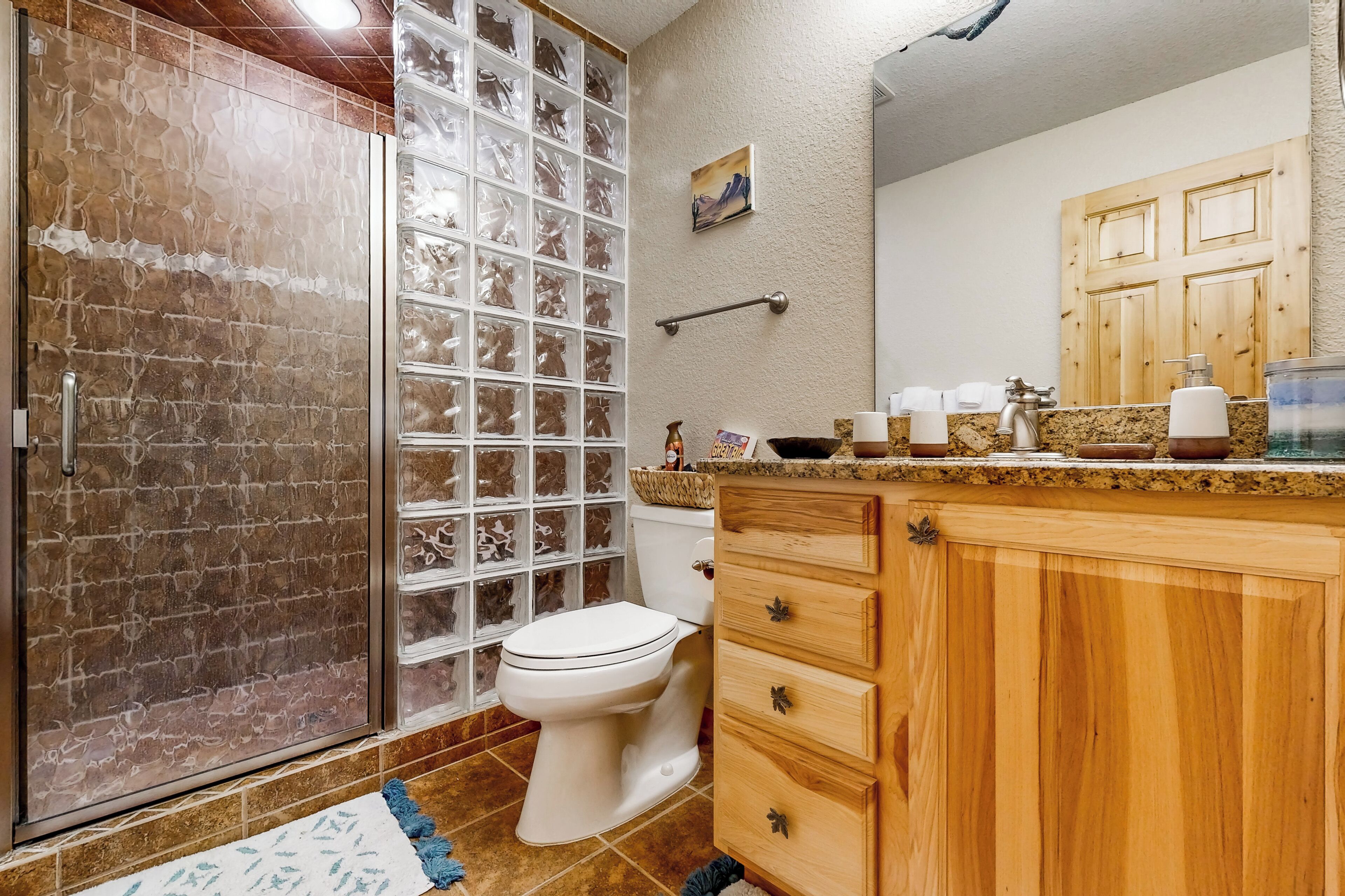 Un baño con cabina de ducha de vidrio, inodoro blanco, armarios de madera y encimera de granito.