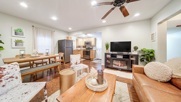 A modern living room with a wooden dining table, a sofa, a TV, and a ceiling fan. - Walk to Gotl Strip! Family Cottage w/ Laundry (Geneva)