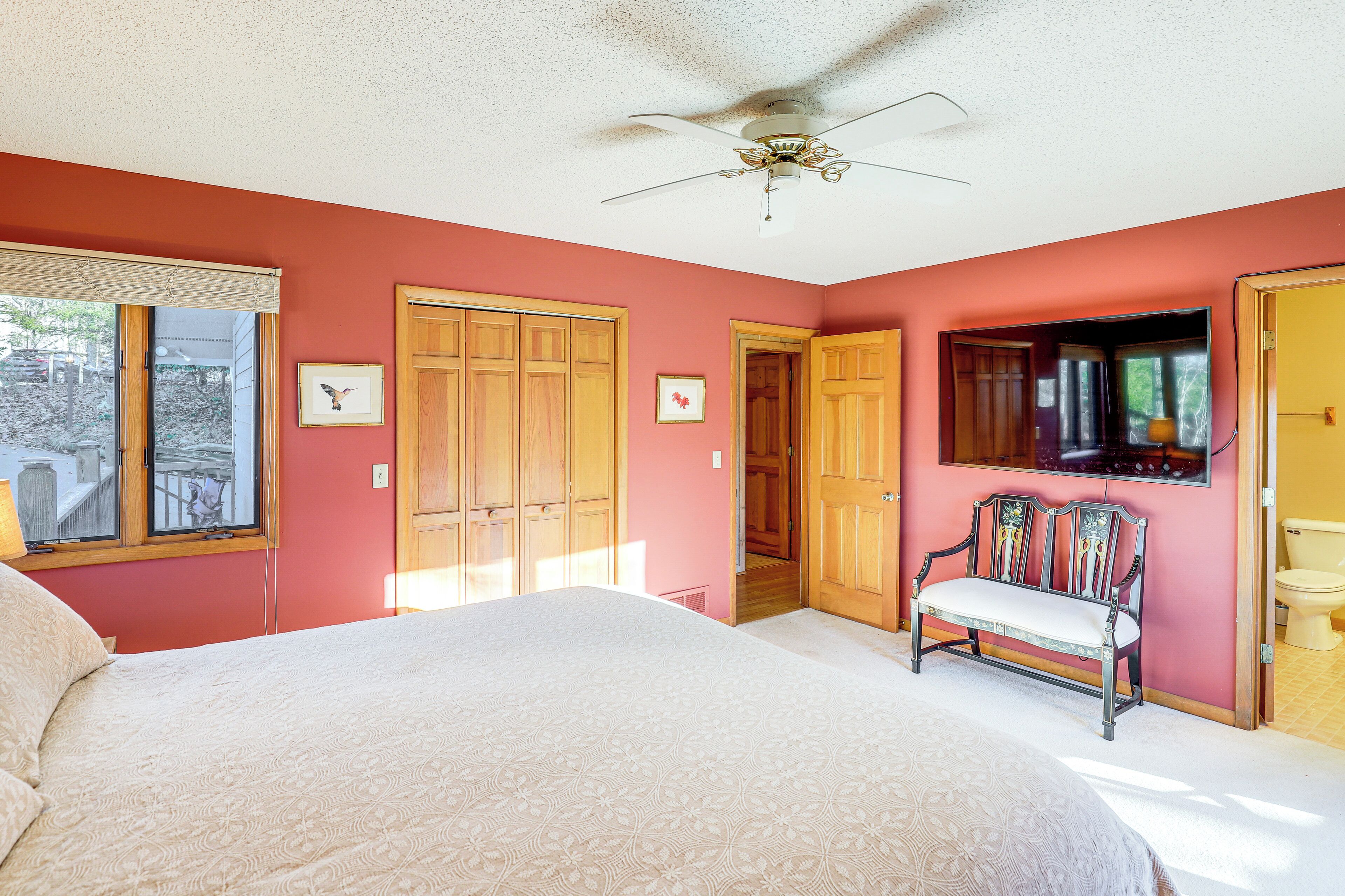 A bedroom with a large bed, wooden wardrobe, a bench, and a ceiling fan.