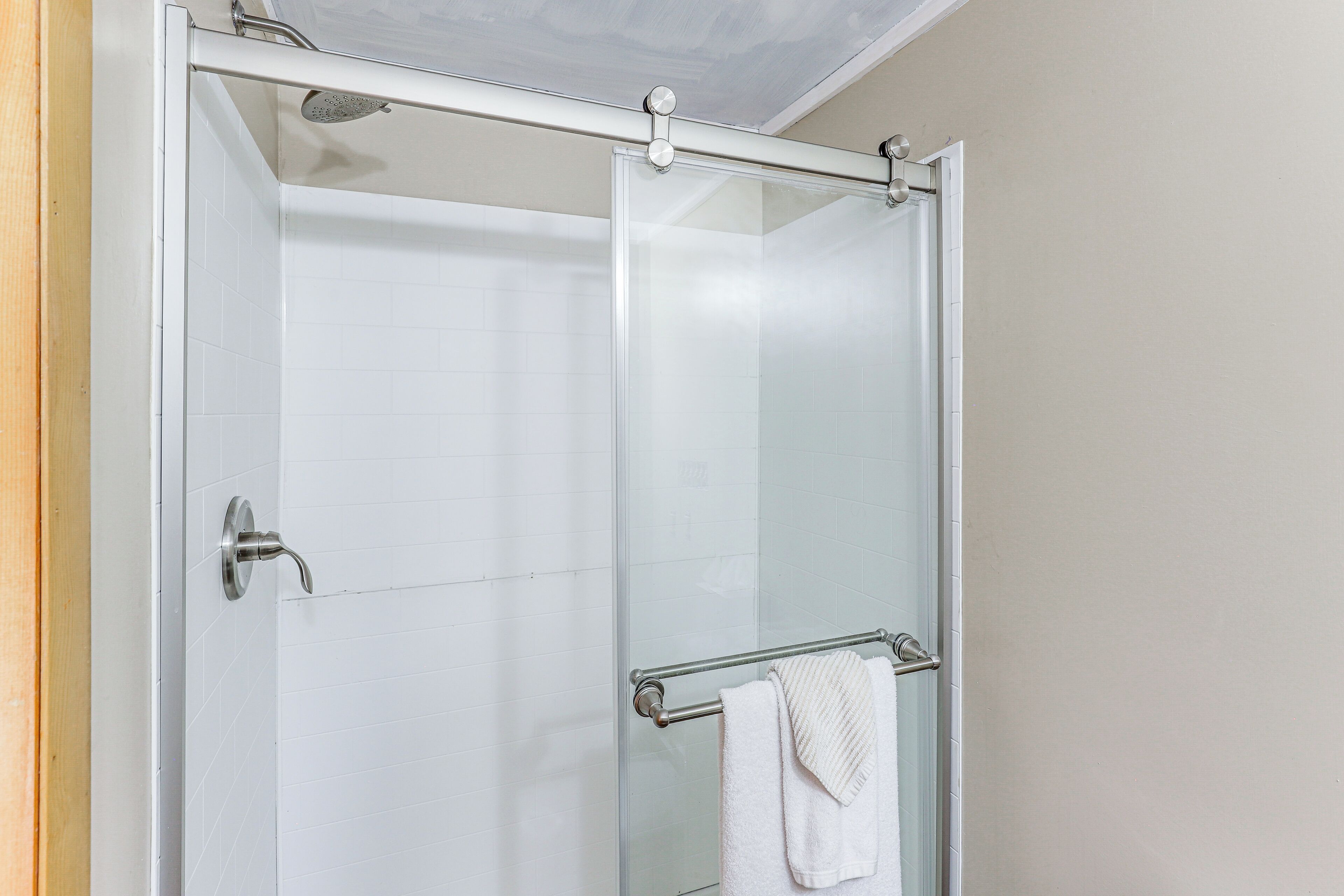 A glass-enclosed shower with a handheld showerhead, a towel rack, and a glass door.