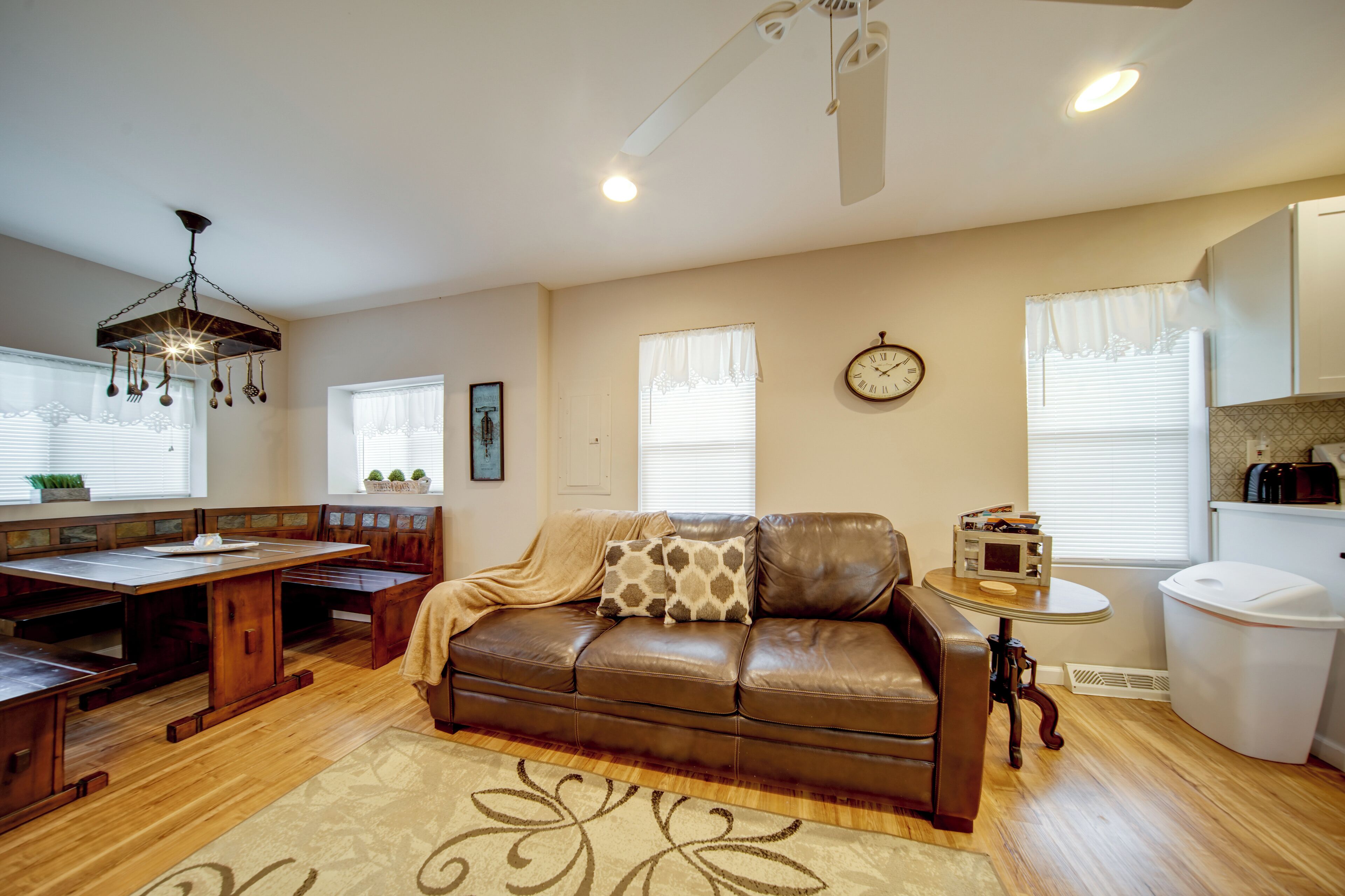 A cozy living room with a brown leather sofa, a wooden dining table, and a chandelier.