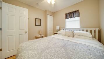 A bedroom with a large bed, a ceiling fan, a window with curtains, and a door.