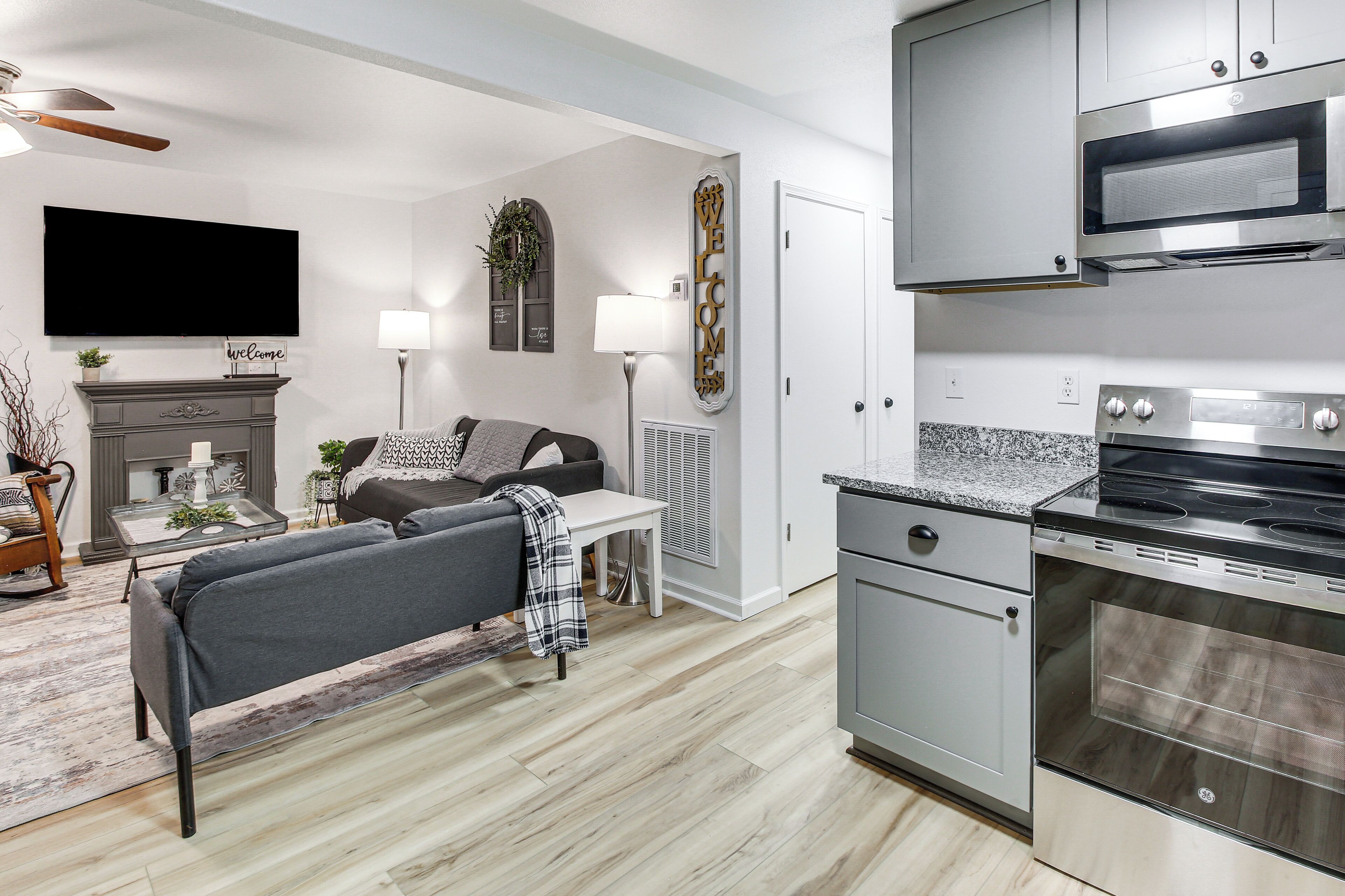 A modern kitchen with a built-in oven and microwave, a grey sofa, a fireplace, and a flat-screen TV.
