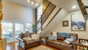 A spacious living room with two leather sofas, a wooden staircase, and a large window with blinds. - Waterfront Family Getaway in Lake Ozark w/ Dock (Lake Ozark)