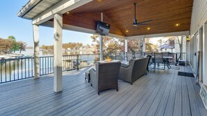 A covered outdoor deck with wooden flooring, wicker furniture, and a TV mounted on the ceiling. - Waterfront Family Getaway in Lake Ozark w/ Dock (Lake Ozark)