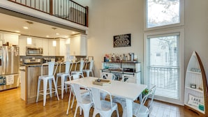 A modern kitchen with white cabinets, a dining area with white chairs, a bar area with bottles, and a large window with blinds. - Waterfront Family Getaway in Lake Ozark w/ Dock (Lake Ozark)