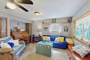 Un soggiorno con un divano blu, un baule verde, un pianoforte in legno e una ventola a soffitto.