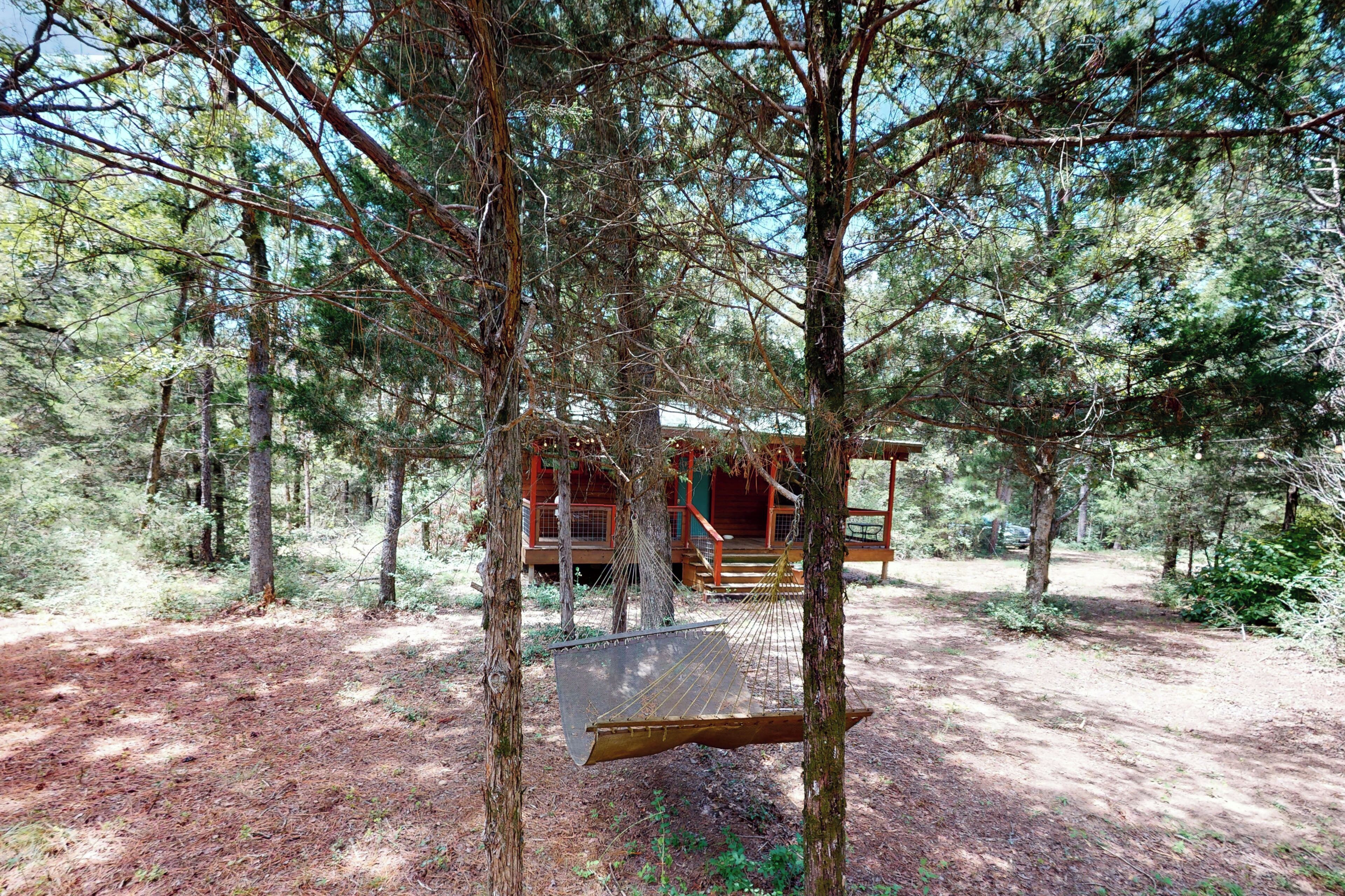 A cabin surrounded by trees with a hammock hanging between two trees.