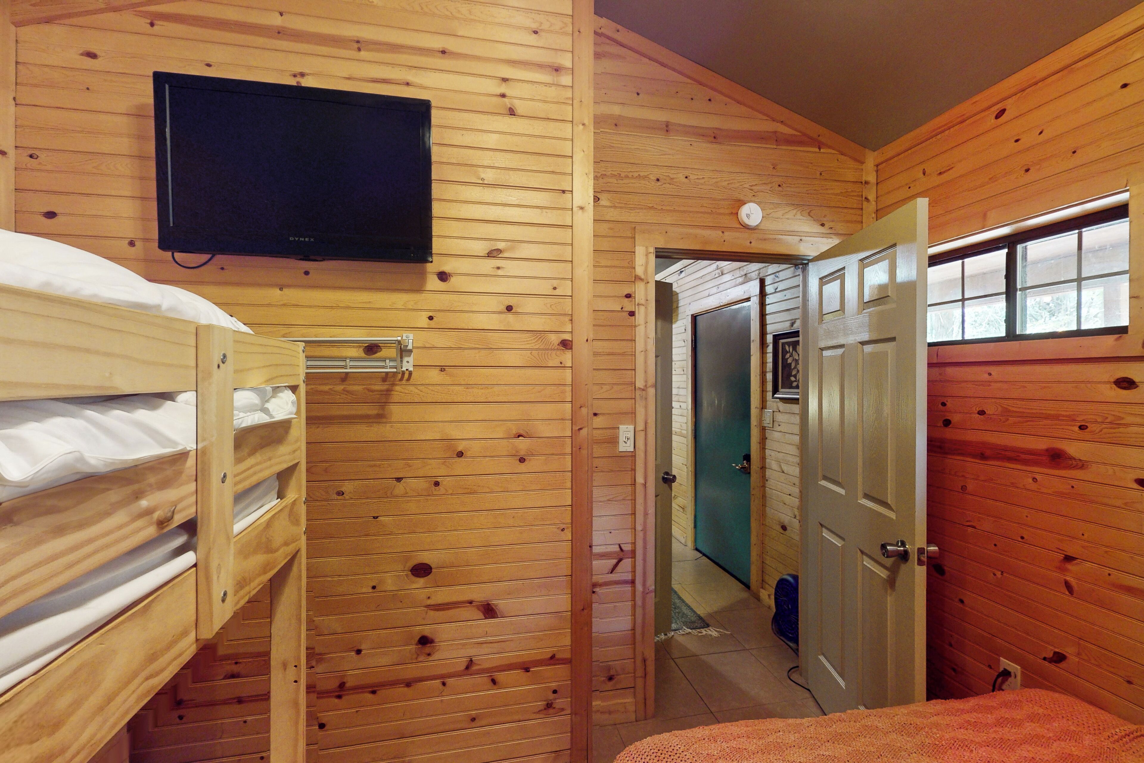 Une pièce de cabane en bois avec des lits superposés, une télévision et une porte donnant sur une autre pièce.