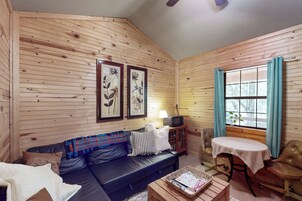 Interior acogedor de una cabaña con pared de madera, sofá de cuero, una mesita y ventana con cortinas.