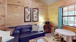 A cozy cabin interior with a wooden wall, a leather sofa, a small table, and a window with curtains. - Serene & Secluded Paige Cabin: Dogs Welcome! (Paige)
