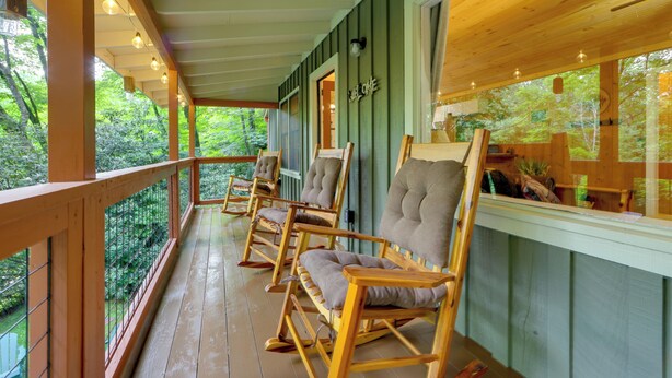 A wooden porch with rocking chairs, a wooden railing, and a view of greenery. - Quiet Family Cabin in Balsam: Hike, Ski, Explore (Balsam)