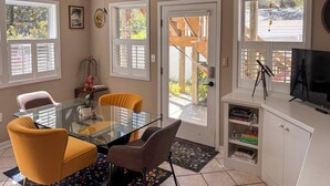 Un coin repas avec une table en verre, deux chaises jaunes, une plante en pot et une vue sur l’extérieur.