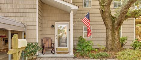 A house with a porch, an American flag, a mailbox, and a tree.