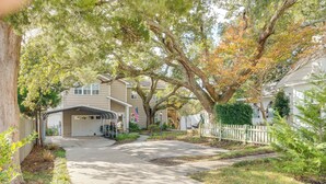 Une allée menant à une maison, qui aboutit à un garage doté d’un abri-voiture, le tout entouré d’arbres matures et d’une clôture blanche en bois.