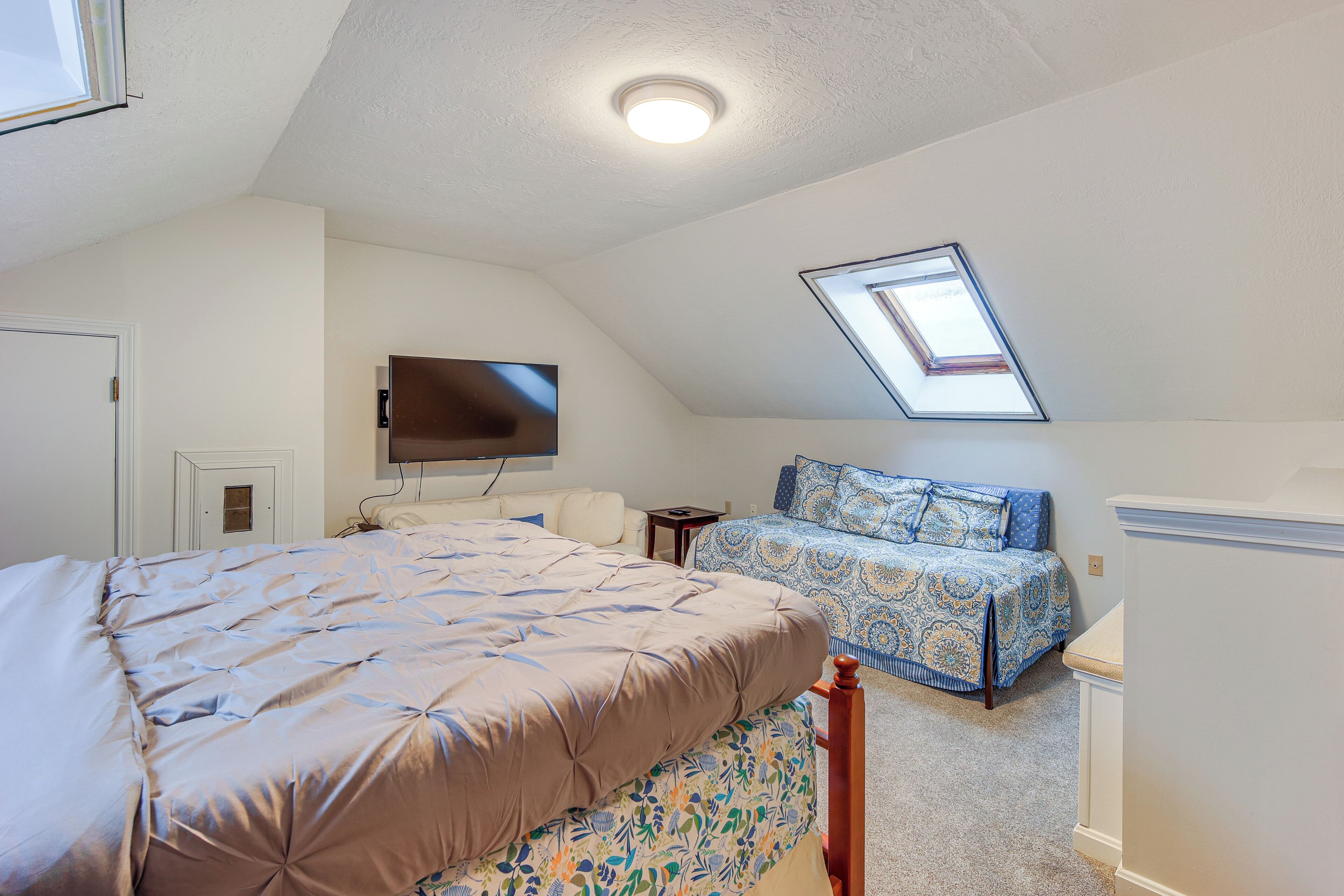 A bedroom with a large bed, a smaller bed, a TV mounted on the wall, and a skylight.