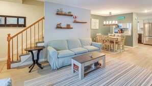 A living room with a sofa, coffee table, and a staircase. There is a kitchen area with a dining table and chairs. - 5 Mi to Loon Mountain Resort! Family Townhome (North Woodstock)