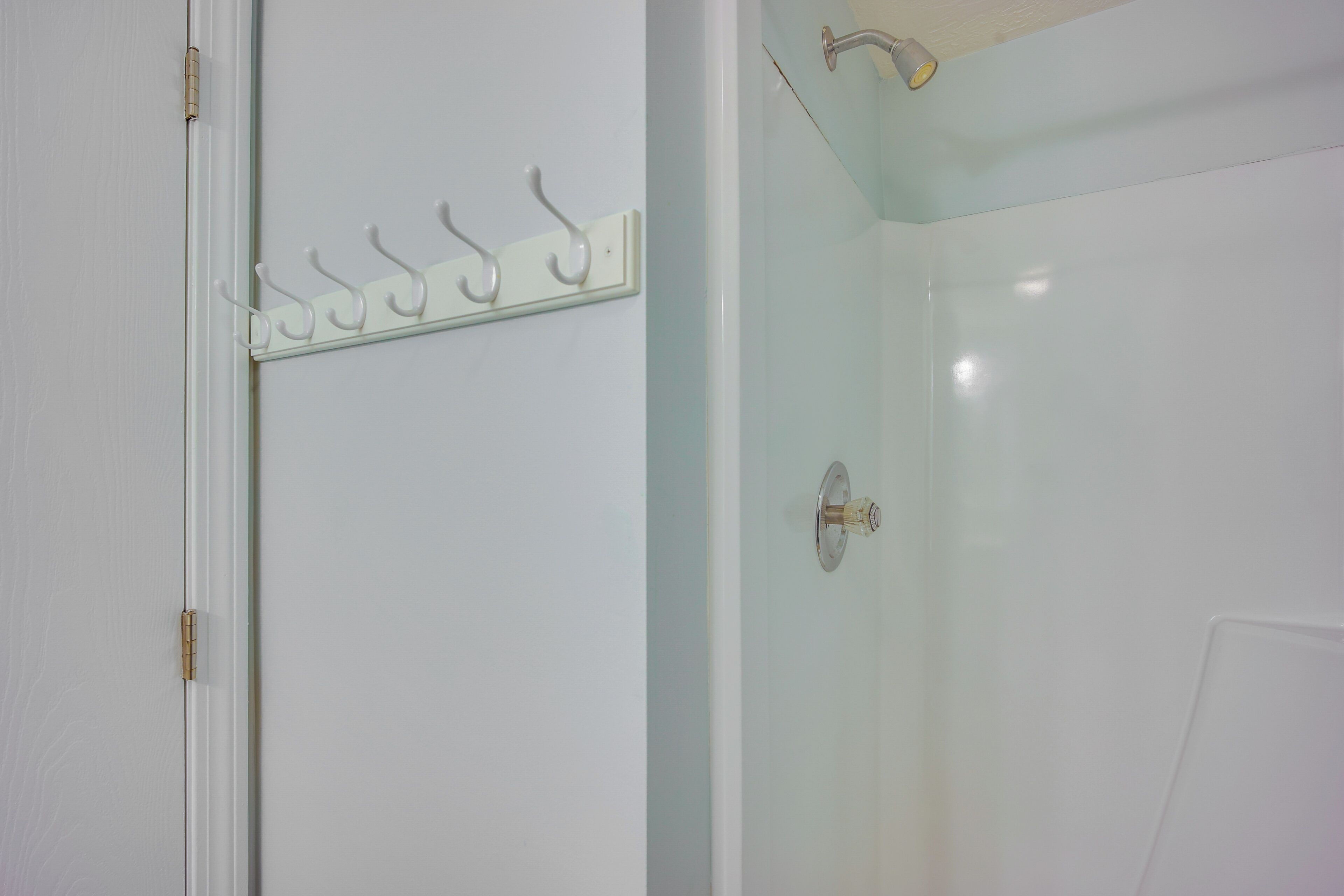 Een badkamer met een glazen douchecabine, een witte deur met een kapstok en een zichtbare handdoekhouder.