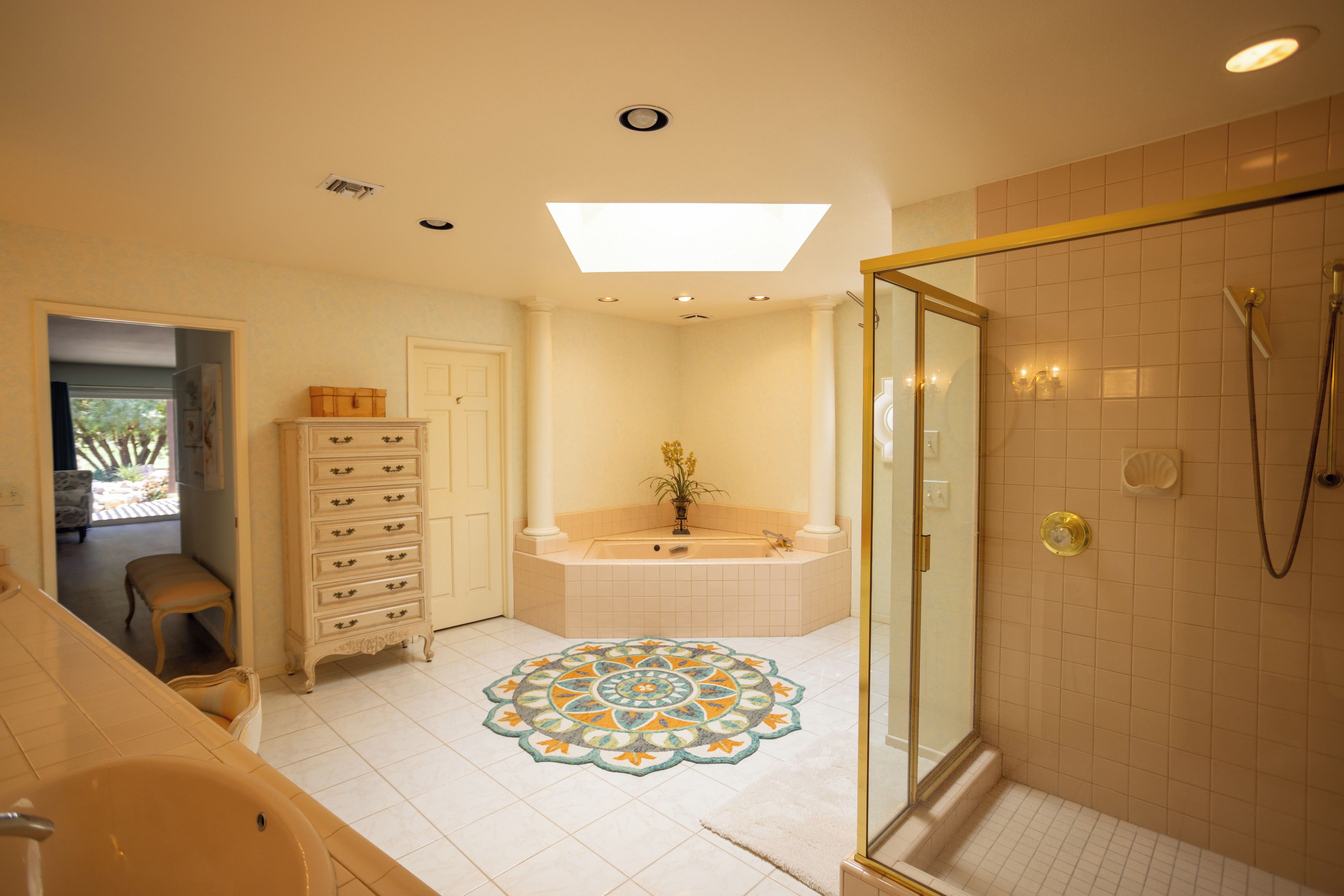 A bathroom with a glass-enclosed shower, a freestanding bathtub, and a decorative floor mat.