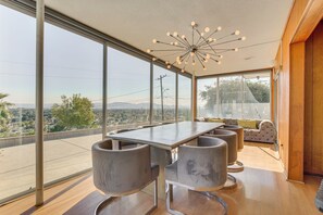 A modern dining area with a large table and chairs, large windows offering a city view, and a unique ceiling light fixture. - Stunning MCM Escape w/ Mtn Views in San Bernardino (San Bernardino)