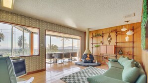 A modern living room with a fireplace, a sofa, a television, and a dining area with a view. - Stunning MCM Escape w/ Mtn Views in San Bernardino (San Bernardino)