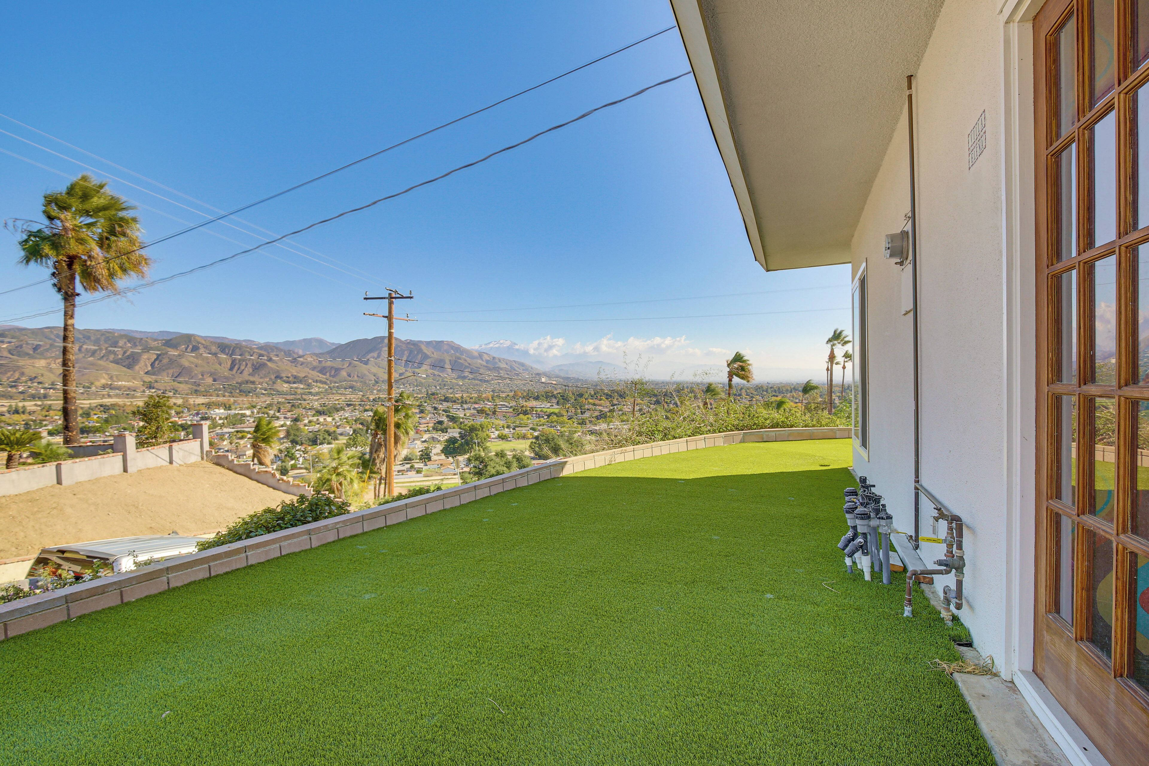 A balcony with artificial grass, a view of a cityscape and mountains, and a building with large windows.