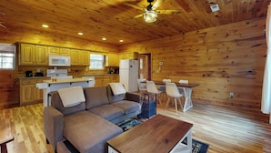 Een gezellig interieur van een vakantiehuisje, met een houten plafond, een bank, een eettafel en een keukenhoek.
