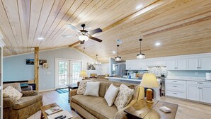 A spacious living room with a wooden ceiling, a sofa, a coffee table, and a dining table. - Historic Barn in Mississippi: Equestrian Getaway! (Tylertown)